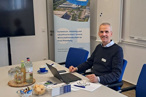 Ein Mann sitzt an einem Tisch in einem Konferenzraum. Vor ihm liegen Flyer ausgebreitet.