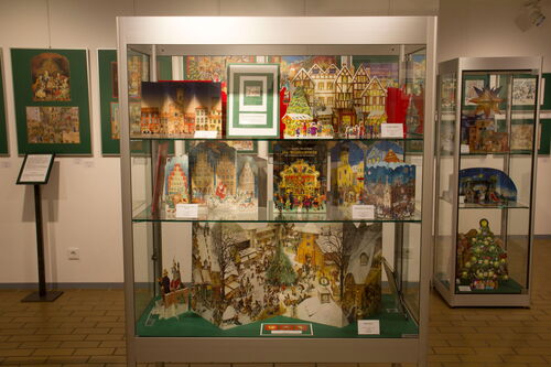 Glasvitrine in einem Museum. In der Vitrine stehen viele unterschiedliche Adventskalender.