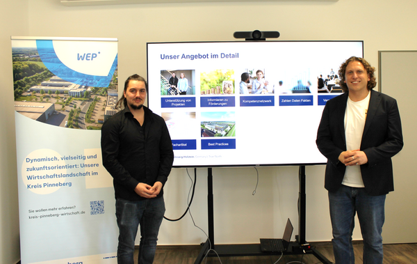 Zwei Männer stehen vor einem Bildschirm. Auf dem Bildschirm ist ihr Beratungsangebot zu Energiethemen für Unternehmen abgebildet.