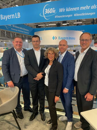 Vier Männer und eine Frau stehen auf einem Messestand und blicken in die Kamera.