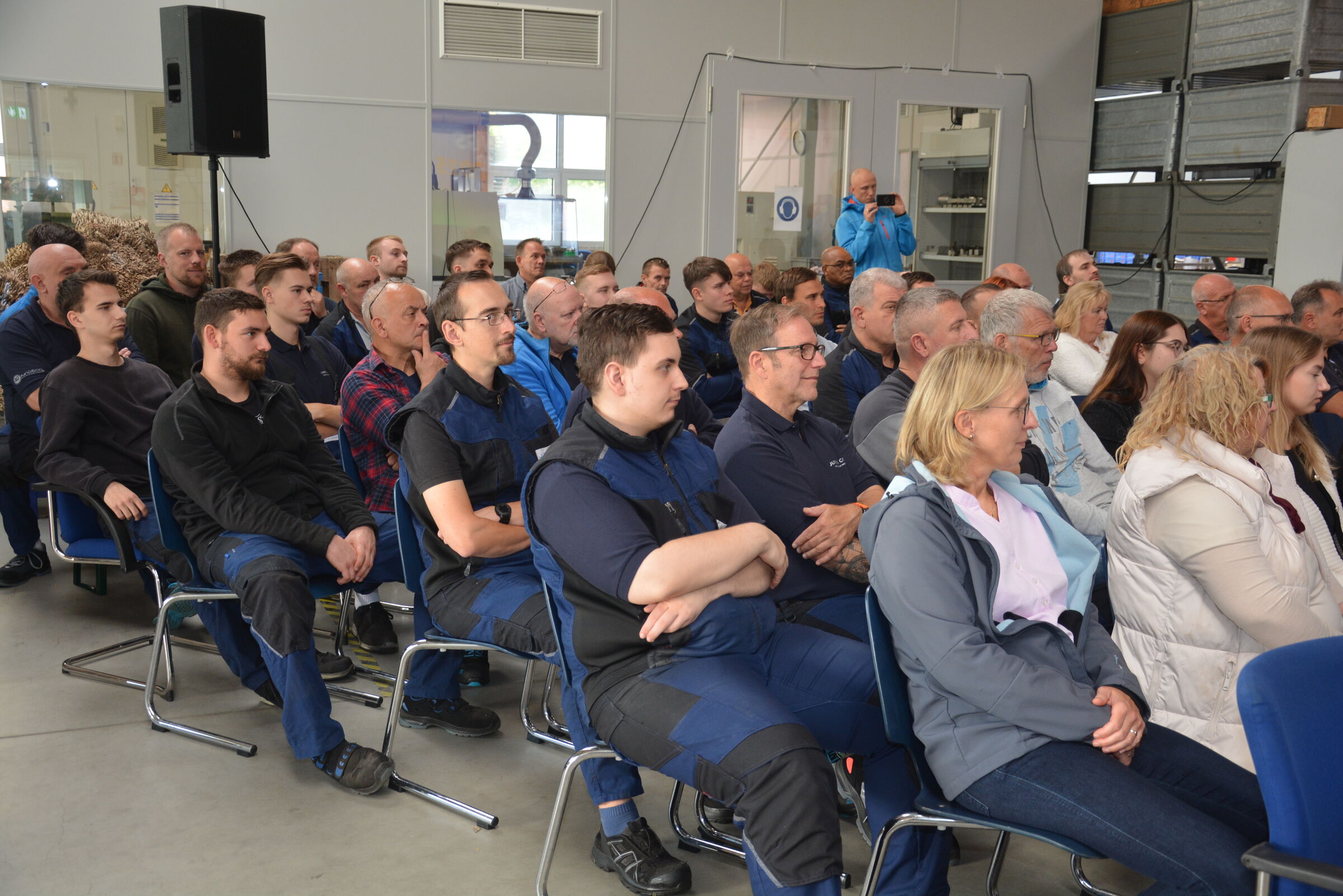 Viele Menschen, die auf Stühlen in Reihen sitzen und den Blick nach vorne richten