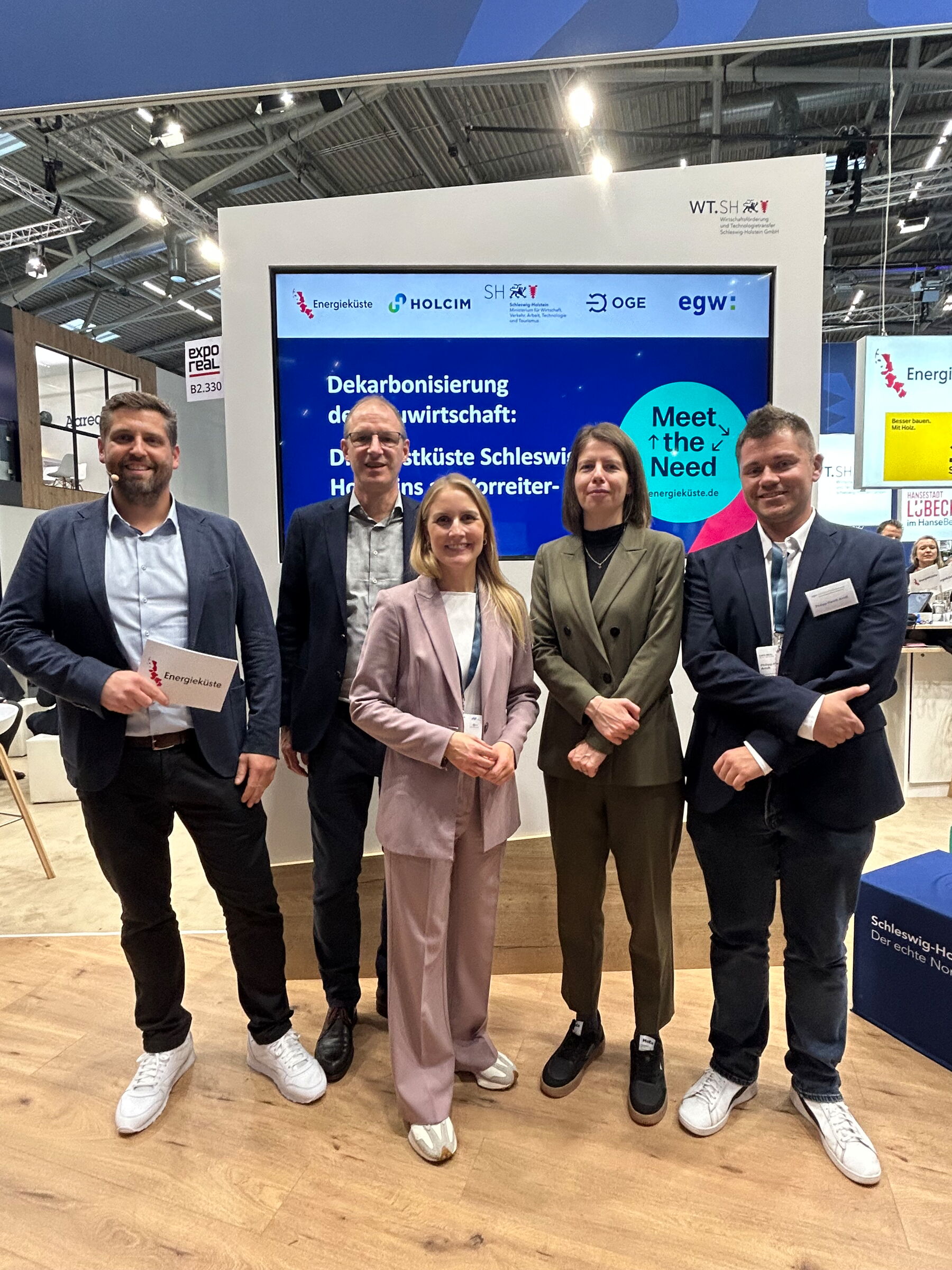 Drei Männer und zwei Frauen stehen vor einem Monitor auf der Messe Expo Real.