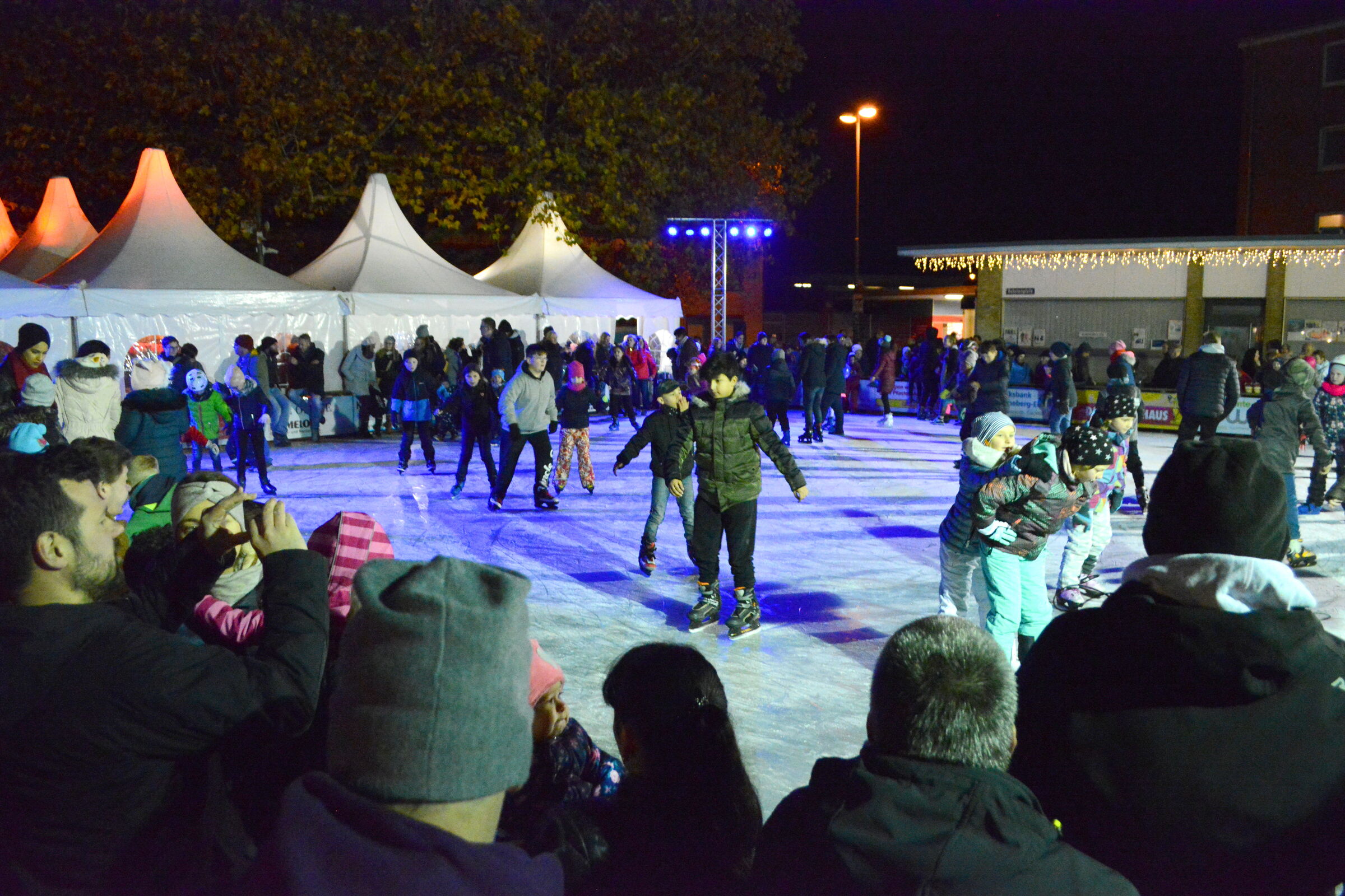 Eisbahn am Abend auf der viele Menschen Eislaufen.