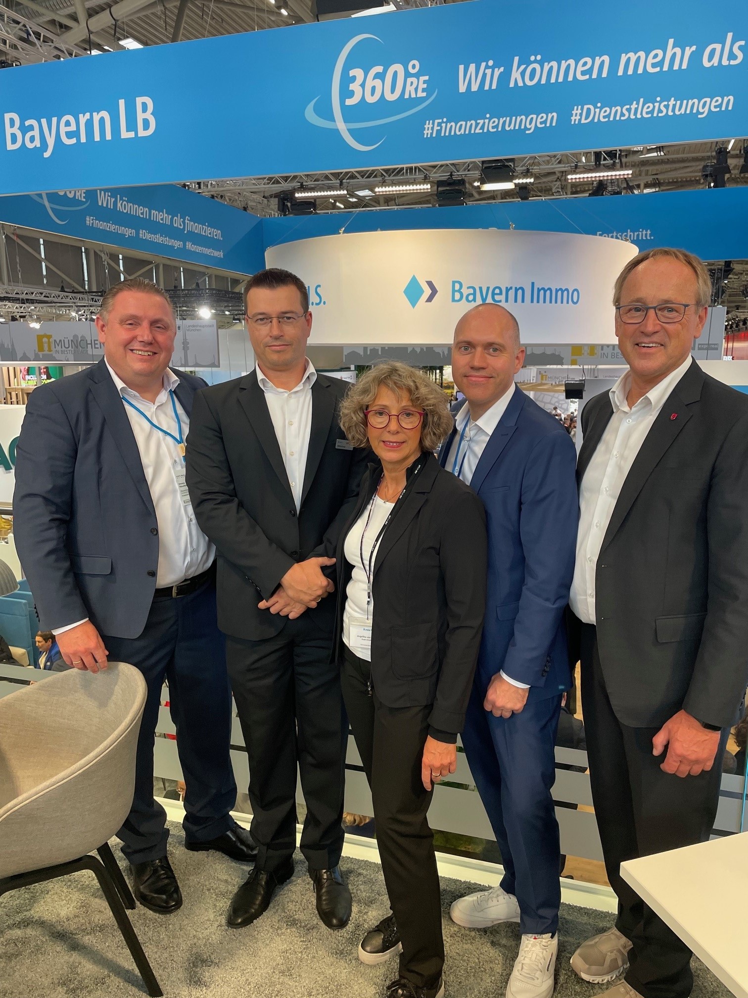 Vier Männer und eine Frau stehen auf einem Messestand und blicken in die Kamera.