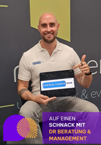 Ein Mann sitzt lächelnd auf einem Stuhl, er hält ein Tablet in den Händen.