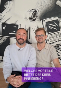 Zwei Männer schauen in die Kamera, sie sitzen vor einer Wand.