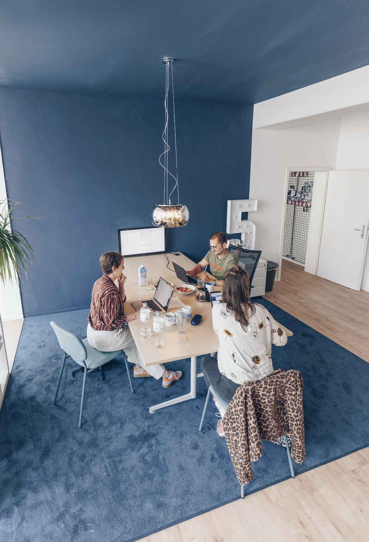 Ein blau gestrichenes Büro, in dem drei Personen an Schreibtischen arbeiten.