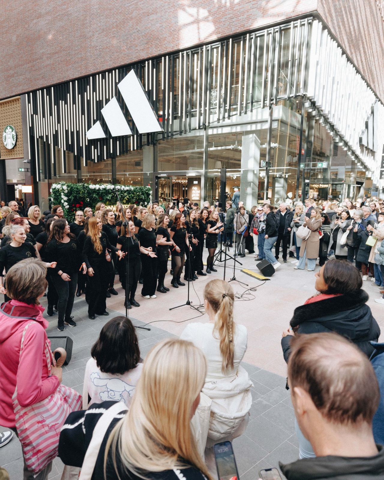 Ein Chor in schwarzer Kleidung singt vor einem Publikum in einem Einkaufszentrum.