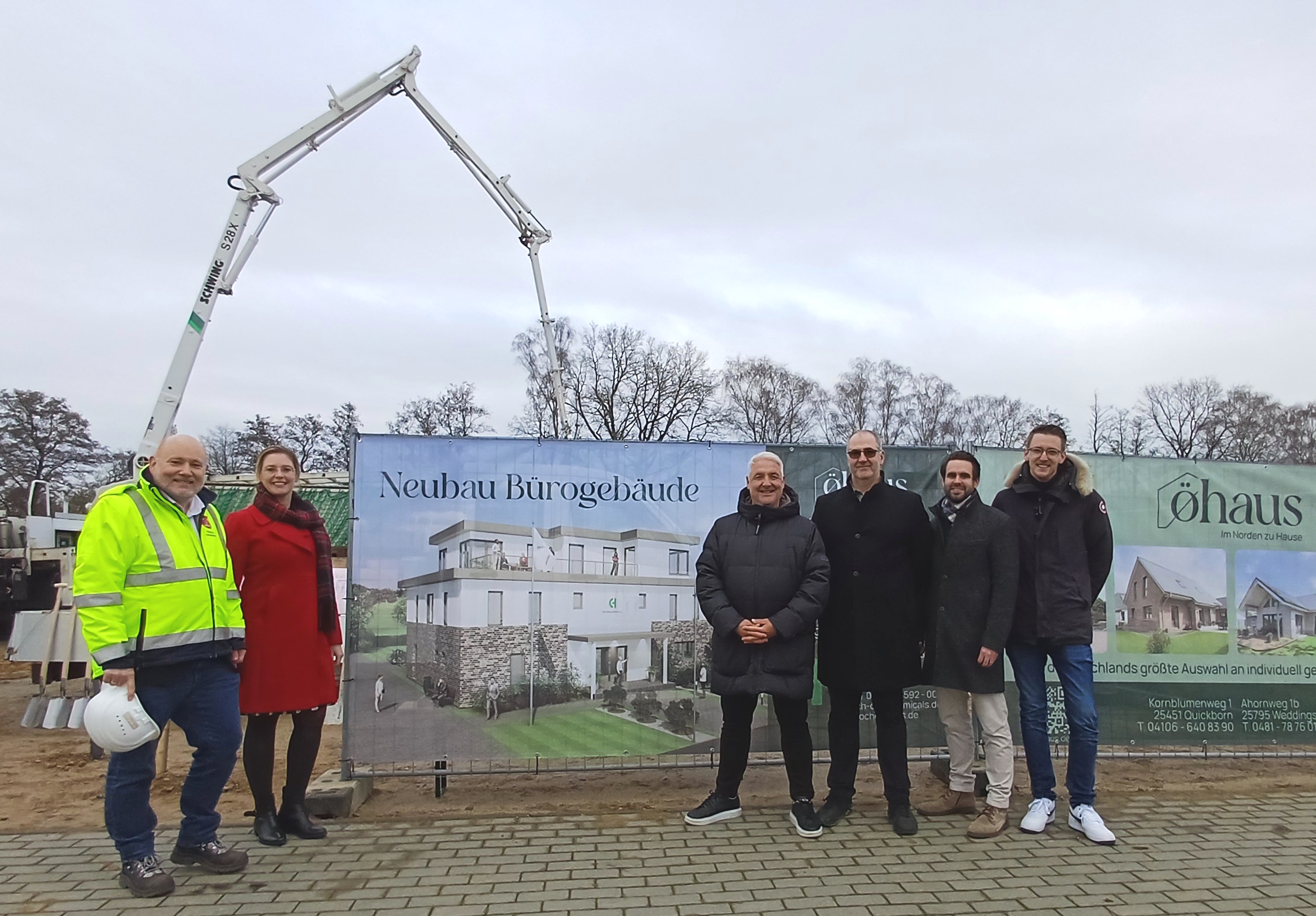 Fünf Männer und eine Frau stehen draußen vor einem Baustellenschild im EQ Businesspark Quickborn.