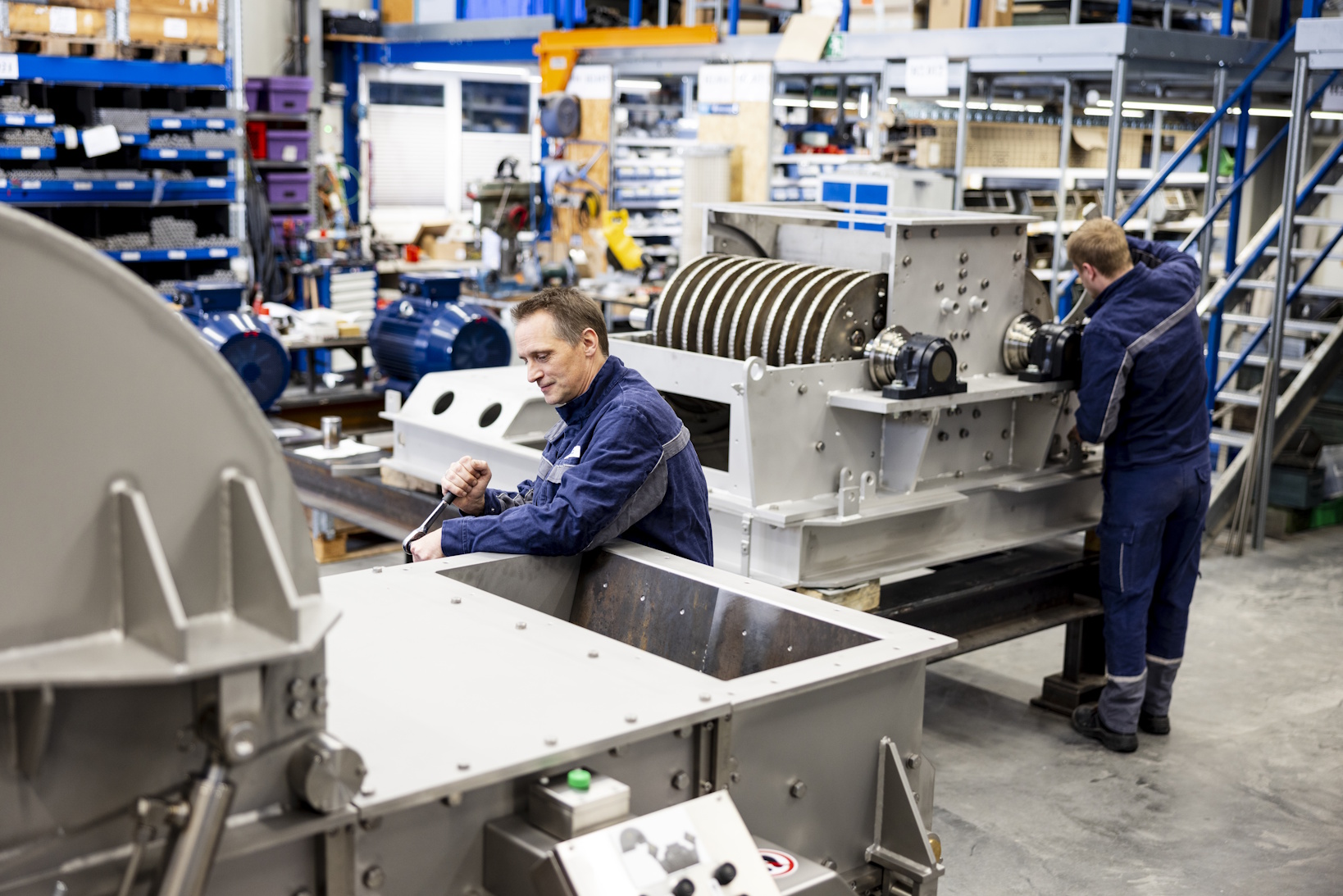 Zwei Männer arbeiten in einer Fabrikhalle an Maschinen zur Bioabfallaufbereitung.
