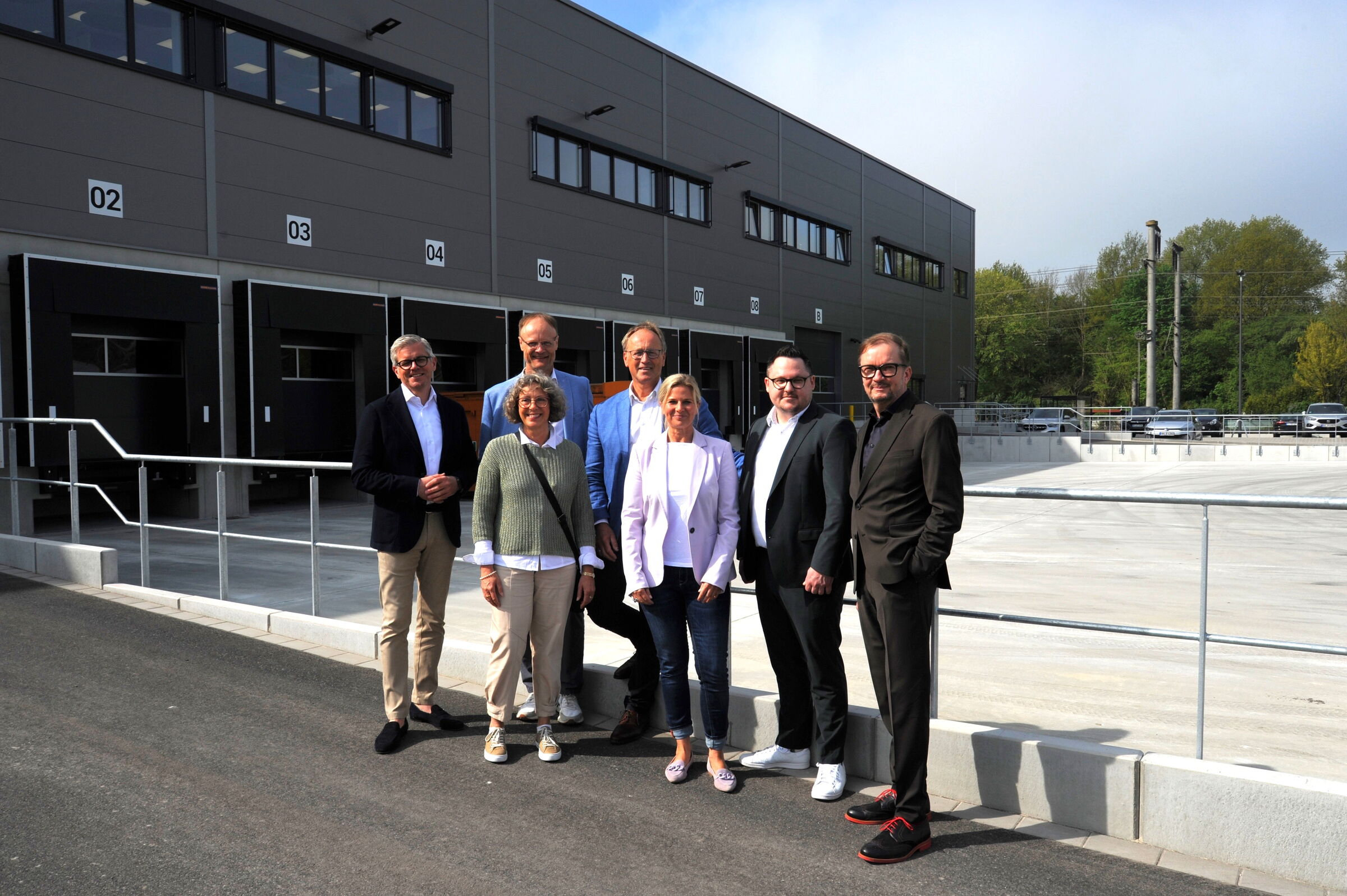 Sieben Personen stehen vor dem neuen Gebäude und blicken Richtung Kamera.