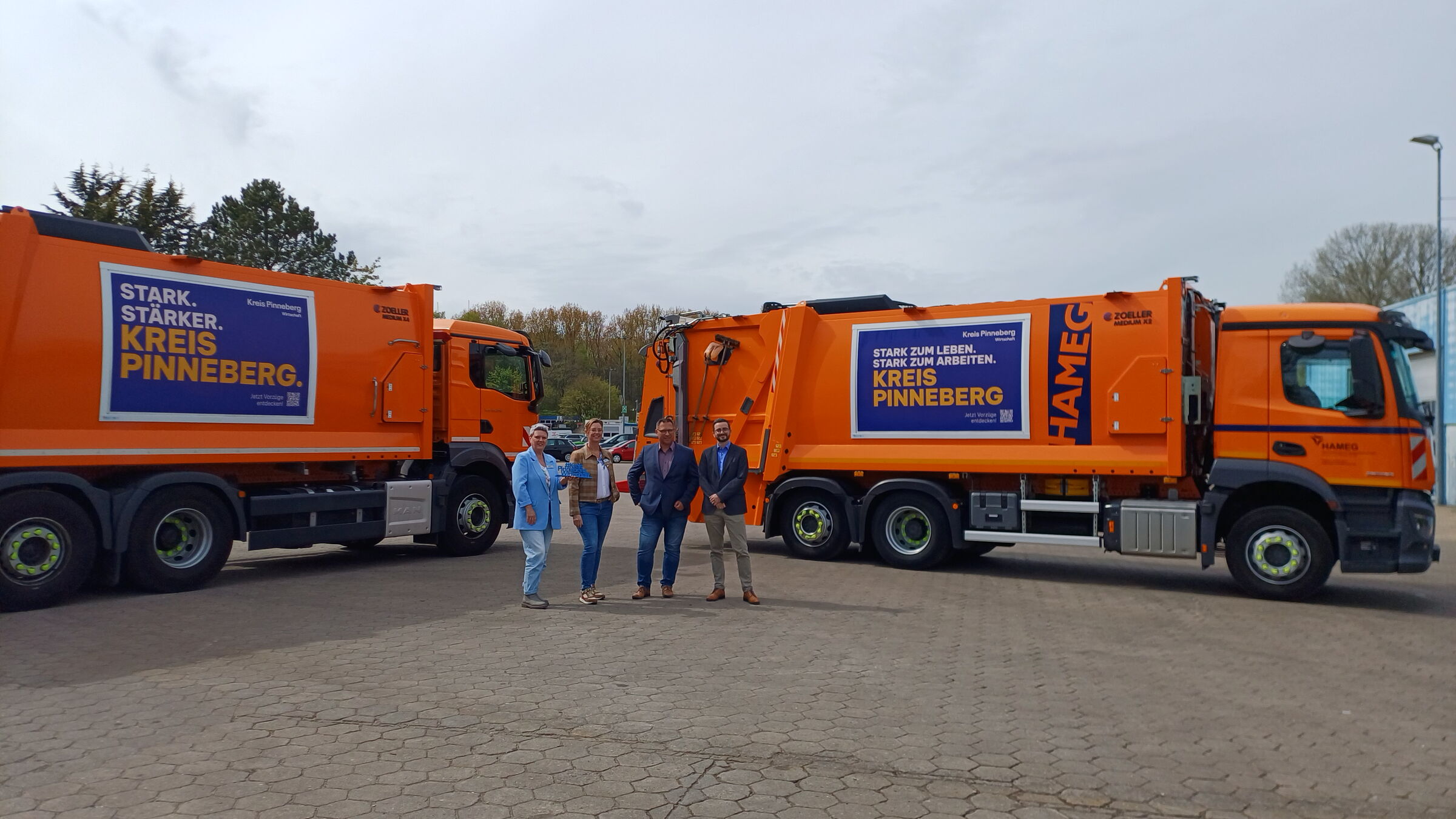 2 orangene Müllfahrzeuge, die mit Werbung des Kreis Pinneberg Wirtschaft beklebt sind und die Verantwortlichen